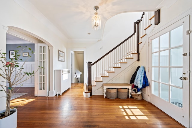 foyer with arched walkways, wood finished floors, french doors, stairway, and ornamental molding