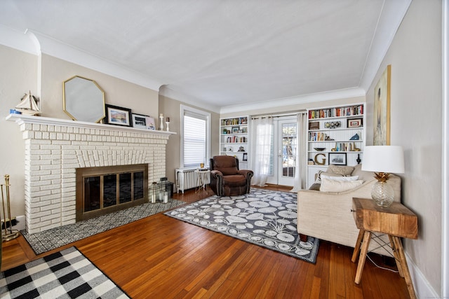 living room with crown molding, a brick fireplace, wood finished floors, and radiator