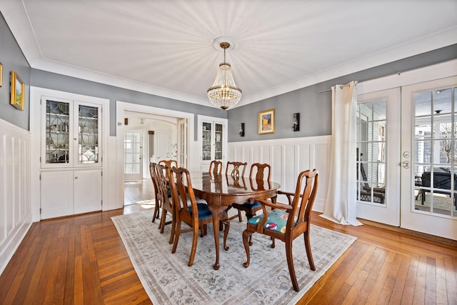 dining room with a decorative wall, wood finished floors, french doors, wainscoting, and an inviting chandelier