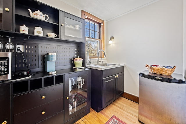 bar featuring light wood finished floors, baseboards, freestanding refrigerator, crown molding, and a sink