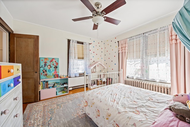 bedroom with multiple windows, ceiling fan, radiator heating unit, and wood finished floors