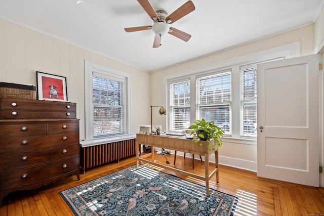 office space with radiator heating unit, wood finished floors, a ceiling fan, and crown molding