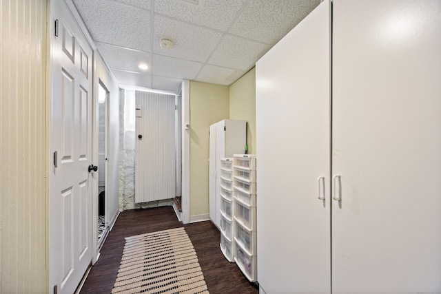 hall with a drop ceiling, dark wood finished floors, and baseboards