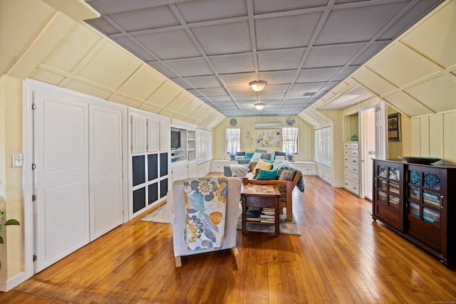 living area featuring built in shelves, lofted ceiling, visible vents, wood finished floors, and coffered ceiling