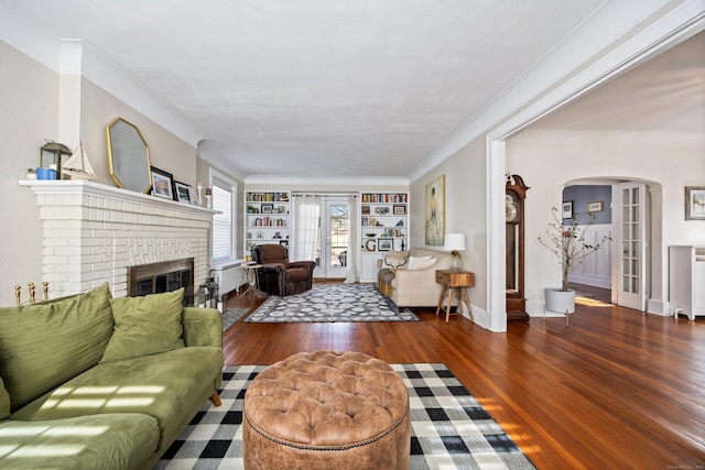 living room with dark wood-style floors, arched walkways, built in features, a fireplace, and ornamental molding