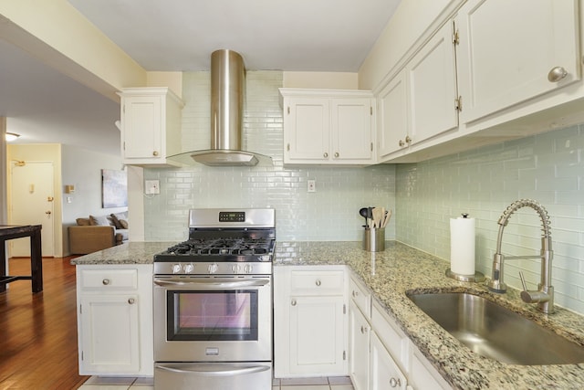 kitchen featuring stainless steel gas stove, light wood-style flooring, a sink, white cabinets, and wall chimney range hood