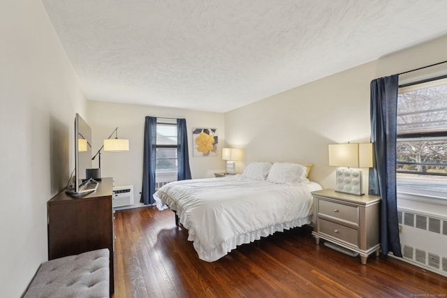 bedroom featuring a wall unit AC, multiple windows, radiator heating unit, and wood-type flooring