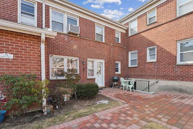 view of exterior entry with cooling unit, a patio area, and brick siding