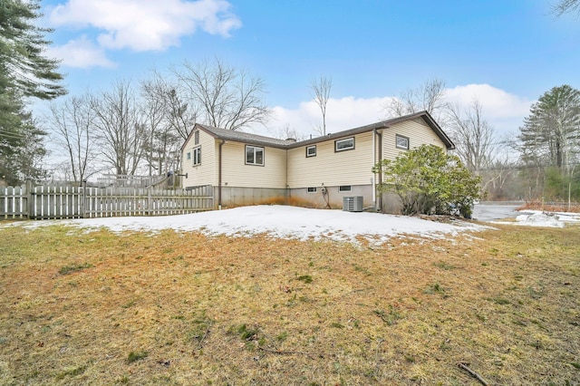 snow covered back of property with fence, a lawn, and central AC unit