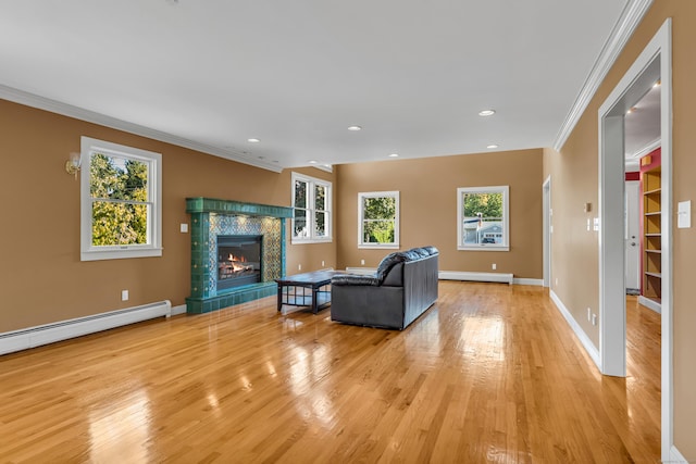 living room with a tile fireplace, a healthy amount of sunlight, crown molding, and light wood-type flooring