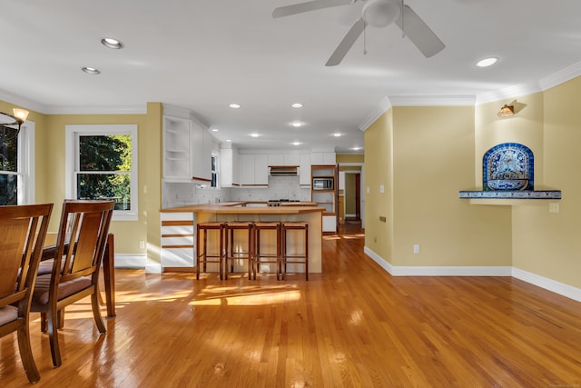 kitchen with white cabinetry, ornamental molding, a kitchen bar, and kitchen peninsula