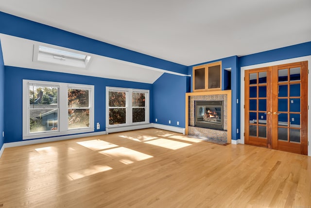 unfurnished living room with vaulted ceiling, a high end fireplace, wood-type flooring, a baseboard radiator, and french doors