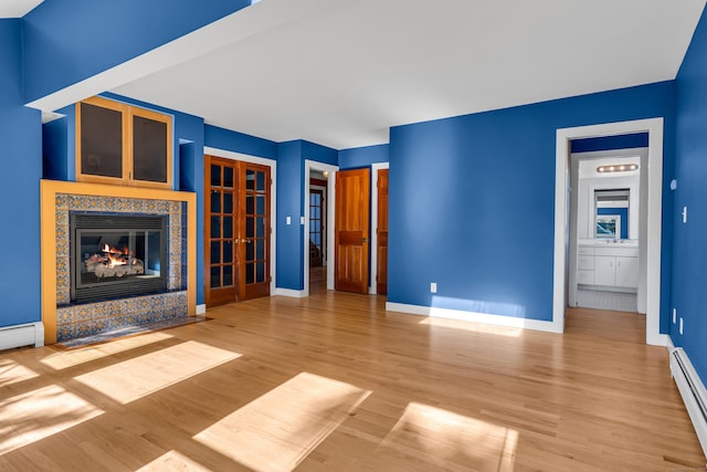 unfurnished living room featuring baseboard heating, a tile fireplace, and hardwood / wood-style flooring