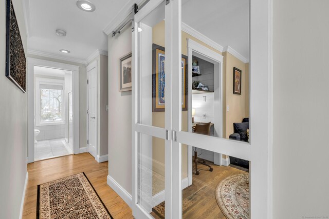 hall featuring a barn door, baseboards, ornamental molding, wood finished floors, and french doors