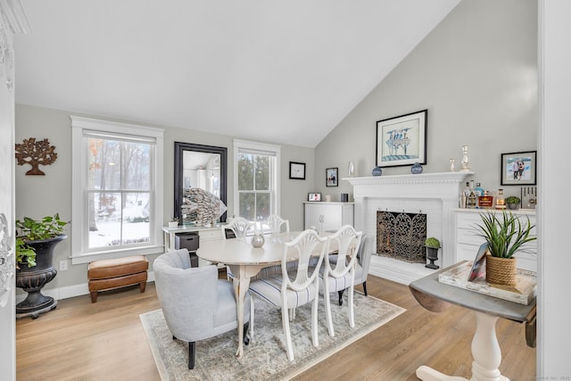 dining room with light wood-style floors, lofted ceiling, a brick fireplace, and baseboards