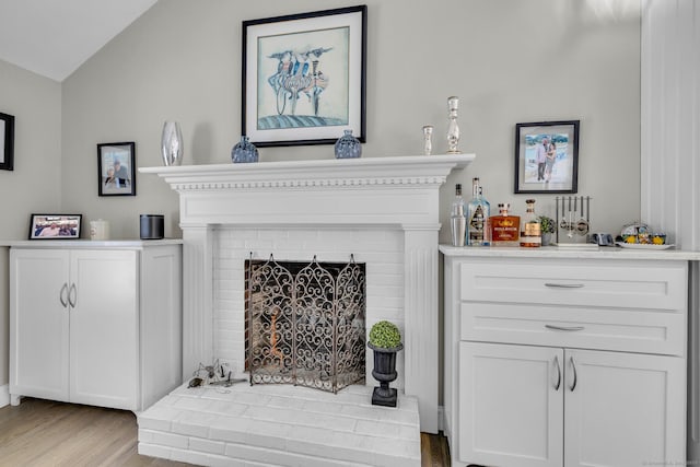 living room featuring lofted ceiling, a bar, a brick fireplace, and light wood-style flooring