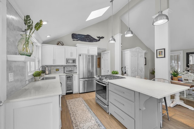 kitchen featuring hanging light fixtures, appliances with stainless steel finishes, white cabinets, a sink, and beverage cooler