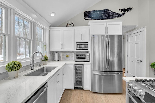 kitchen featuring appliances with stainless steel finishes, white cabinetry, a sink, vaulted ceiling, and beverage cooler