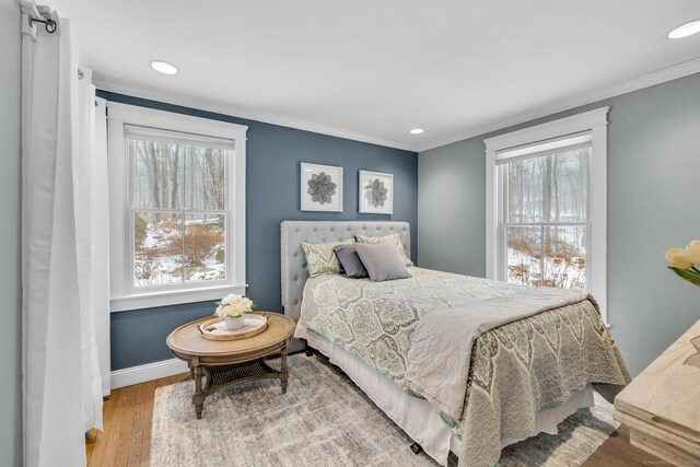 bedroom featuring ornamental molding, multiple windows, baseboards, and wood finished floors