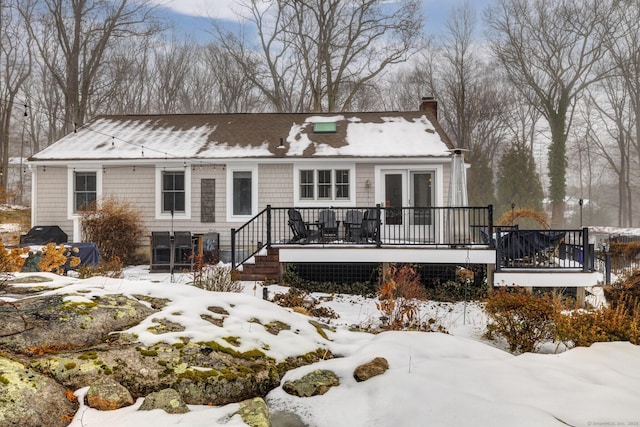 snow covered rear of property featuring a chimney and a wooden deck