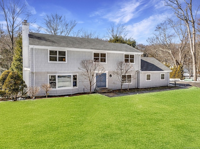 rear view of property with entry steps, a yard, a shingled roof, and a chimney