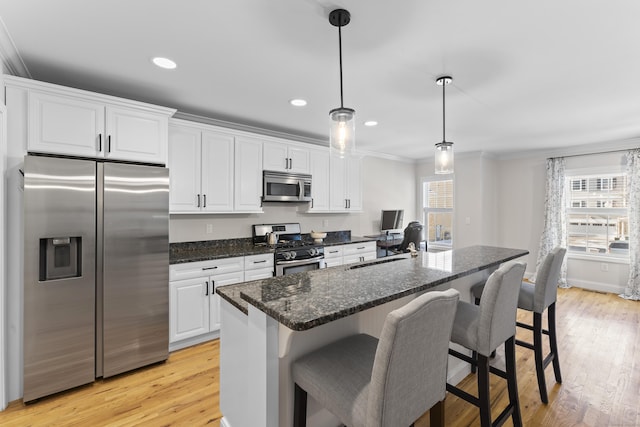 kitchen featuring appliances with stainless steel finishes, pendant lighting, crown molding, white cabinets, and a kitchen island with sink