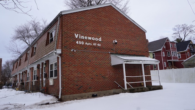 snow covered property featuring brick siding and fence