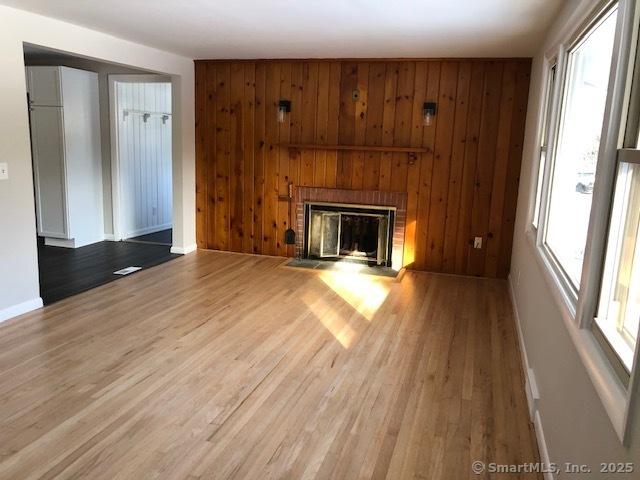 unfurnished living room featuring wooden walls, a brick fireplace, wood finished floors, and a healthy amount of sunlight