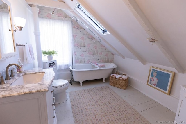 bathroom featuring vanity, toilet, vaulted ceiling with skylight, and a tub to relax in