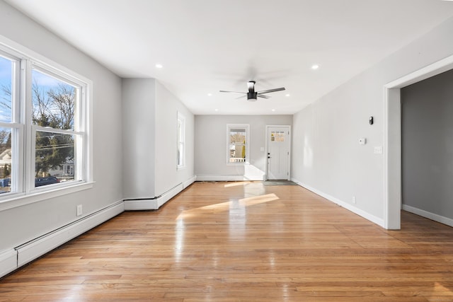 unfurnished living room featuring ceiling fan, a baseboard radiator, light hardwood / wood-style flooring, and a wealth of natural light