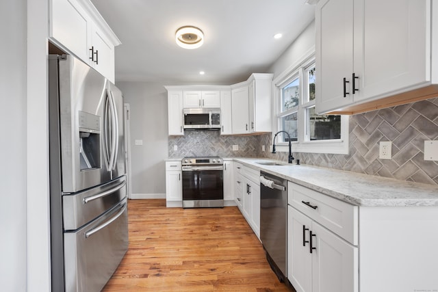 kitchen featuring sink, tasteful backsplash, light wood-type flooring, stainless steel appliances, and white cabinets