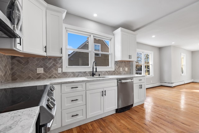 kitchen with sink, appliances with stainless steel finishes, white cabinetry, light stone counters, and light hardwood / wood-style floors