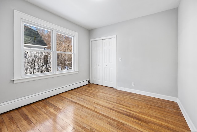 unfurnished bedroom featuring baseboard heating, light hardwood / wood-style floors, and a closet