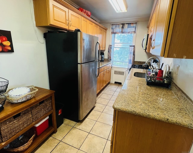 kitchen featuring sink, light stone counters, light tile patterned floors, appliances with stainless steel finishes, and radiator heating unit