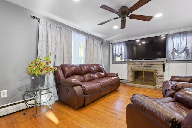 living room with ceiling fan, light wood-type flooring, and a stone fireplace