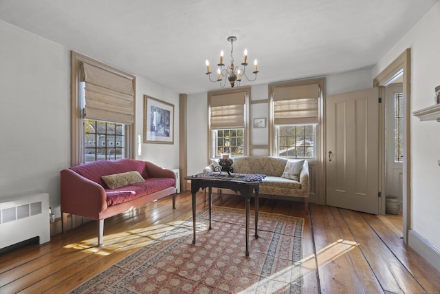 living room with baseboards, wood-type flooring, an inviting chandelier, and radiator heating unit