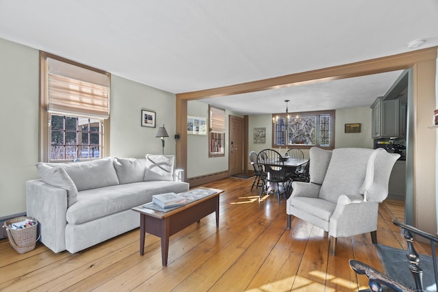 living area with a notable chandelier, light wood-style floors, a wealth of natural light, and a baseboard radiator