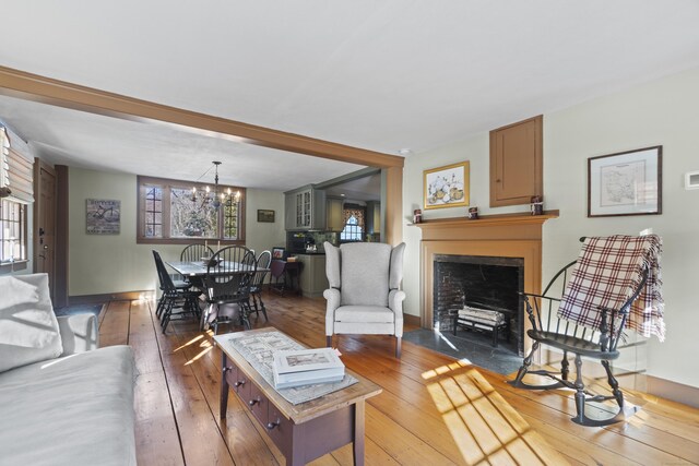 living area with a notable chandelier, a fireplace with flush hearth, plenty of natural light, and hardwood / wood-style flooring