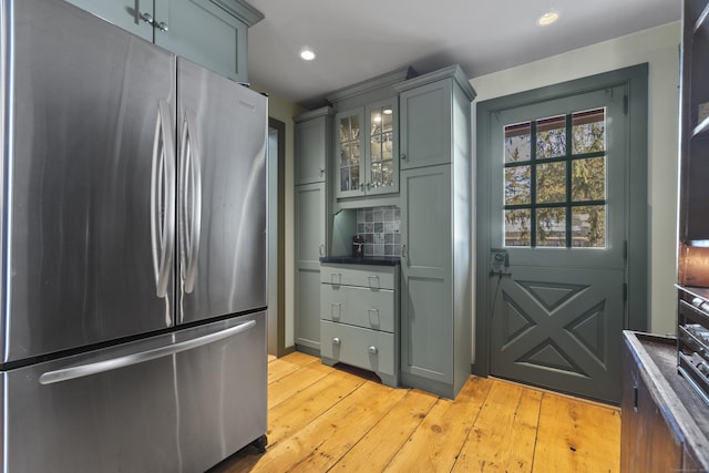 kitchen featuring freestanding refrigerator, glass insert cabinets, light wood-style floors, dark countertops, and tasteful backsplash