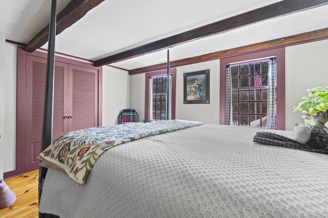 bedroom with a closet, beamed ceiling, and wood finished floors