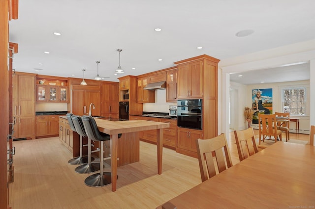 kitchen with stainless steel gas stovetop, decorative light fixtures, black oven, and light hardwood / wood-style flooring