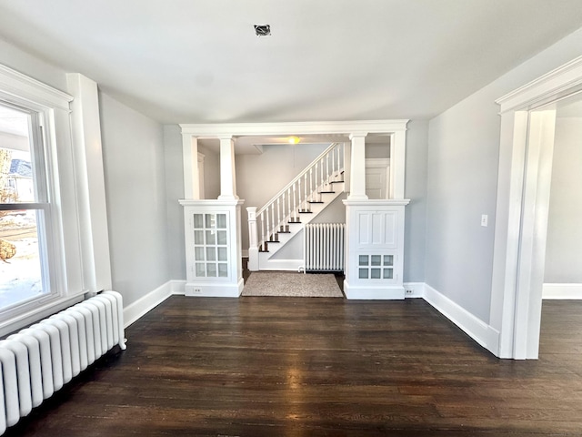 spare room featuring stairs, radiator heating unit, dark wood-style floors, and baseboards