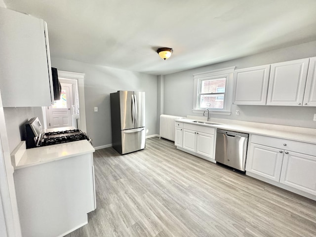 kitchen with stainless steel appliances, radiator heating unit, light countertops, and white cabinetry