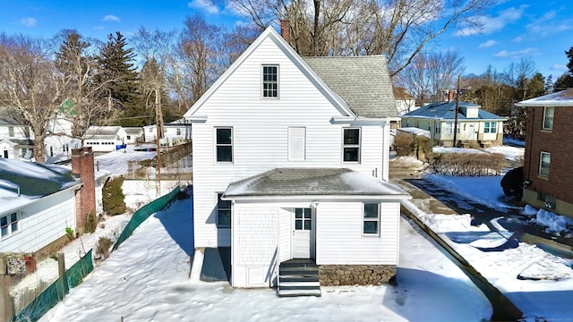 snow covered rear of property with entry steps and a shingled roof