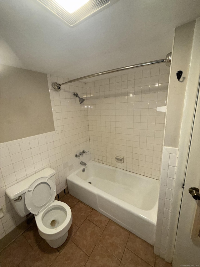 bathroom with tiled shower / bath, toilet, tile patterned flooring, and tile walls