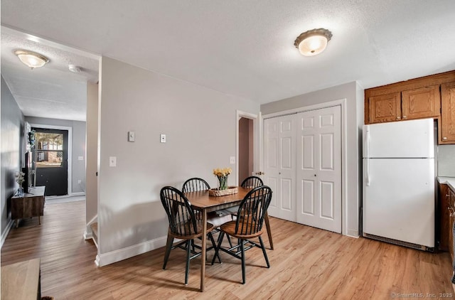 dining room with baseboards, a textured ceiling, and light wood finished floors