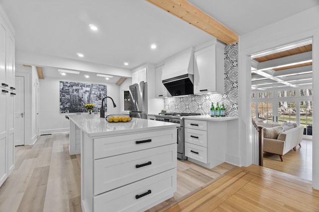 kitchen featuring stainless steel appliances, custom range hood, decorative backsplash, an island with sink, and beamed ceiling