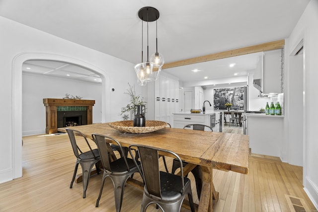 dining room featuring arched walkways, a fireplace, visible vents, light wood-style floors, and beam ceiling