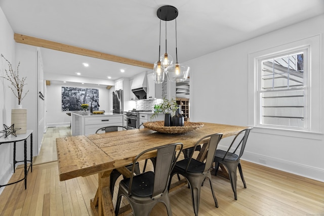 dining space featuring a healthy amount of sunlight, beamed ceiling, light wood-type flooring, and baseboards