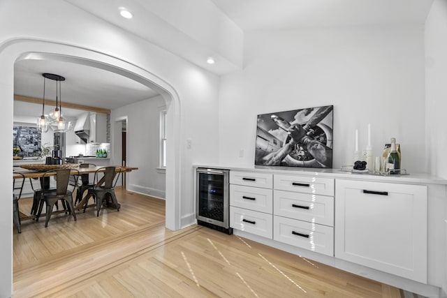 bar featuring beverage cooler, baseboards, arched walkways, hanging light fixtures, and light wood-type flooring